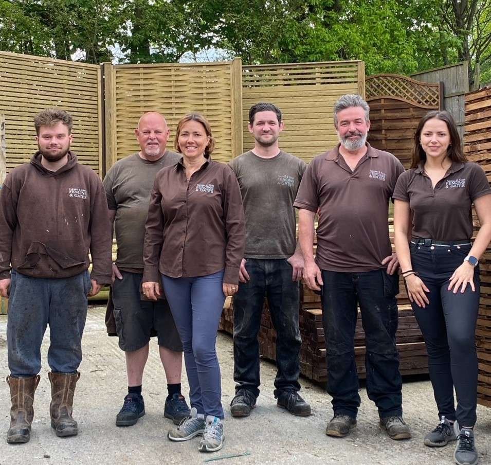 The small team of Tarmec and Croft Fencing and gates working including family and earls colne locals working in our workshop, on site team and in reception. All 6 staff members stood in our well stocked yard of wooden fence panels and fencing materials, wearing out tarmec and croft fencing and gates uniform