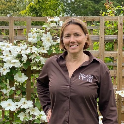 Image of the female company director of our family business in earls colne in front of our wooden trellis panels covered in white flowers. Jane is wearing her tarmec and croft fencing and gates brown uniform